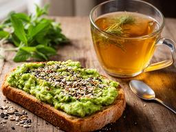Tosta de abacate com sementes ao lado de uma infusão digestiva numa mesa de madeira